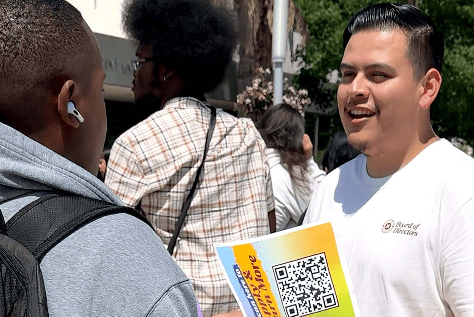 A student board member shakes hands with another person on the outdoor patio.